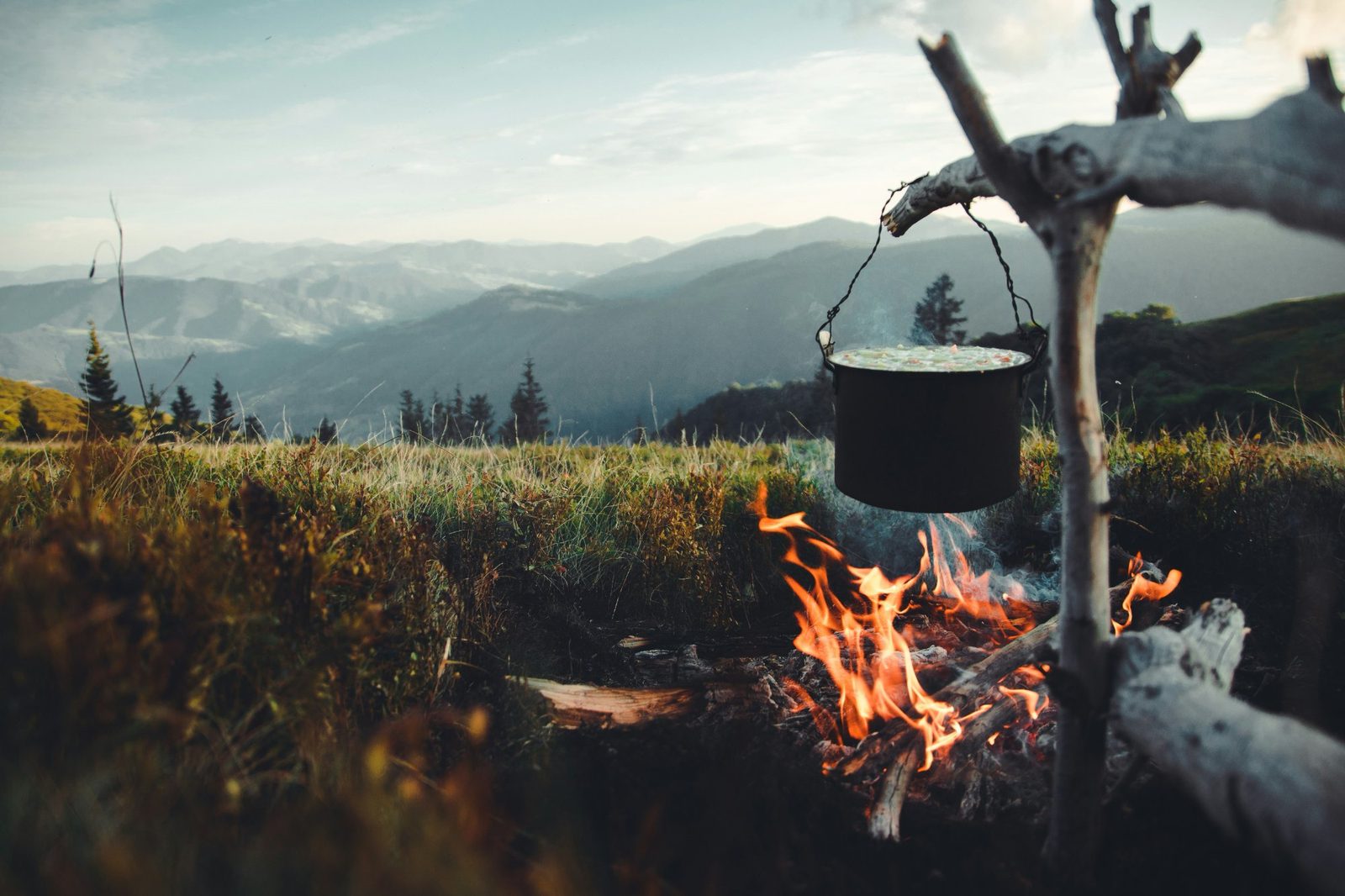 A pot cooking over an open fire with mountain views